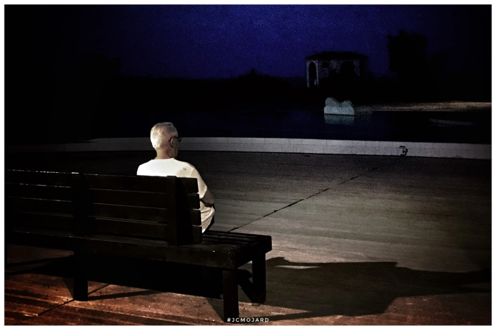 Un homme assis sur un banc dans la nuit de Port Leucate, regarde vers le large.